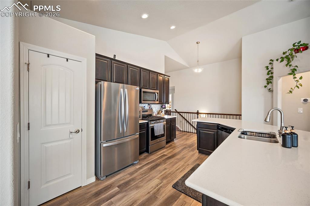 Kitchen featuring stainless steel appliances, dark brown cabinets, decorative light fixtures, lofted ceiling, and dark wood-style flooring