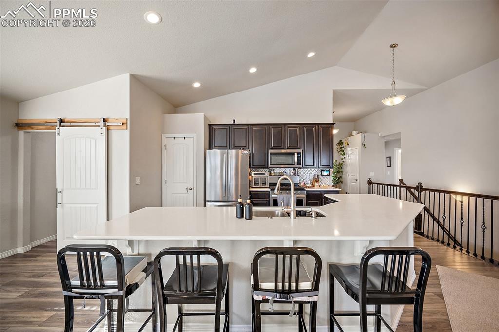 Kitchen featuring a barn door, dark brown cabinets, appliances with stainless steel finishes, dark wood-style floors, and vaulted ceiling