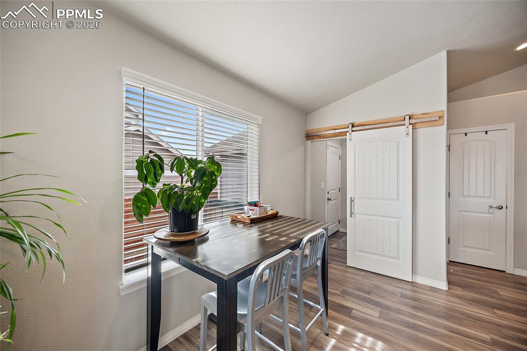Dining room with a barn door, vaulted ceiling, and wood finished floors