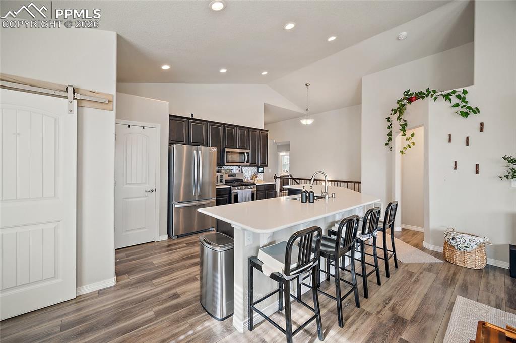 Kitchen featuring stainless steel appliances, a barn door, a kitchen breakfast bar, dark brown cabinets, and a kitchen island with sink