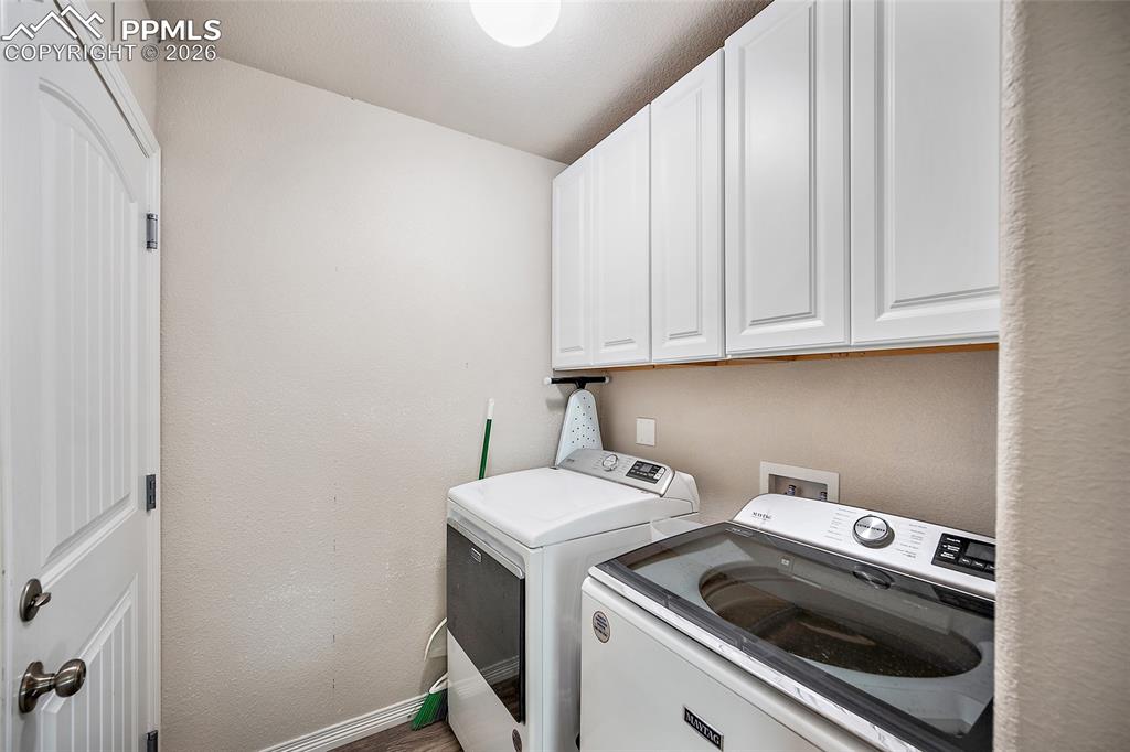 Washroom with cabinet space, washing machine and dryer, and a textured wall