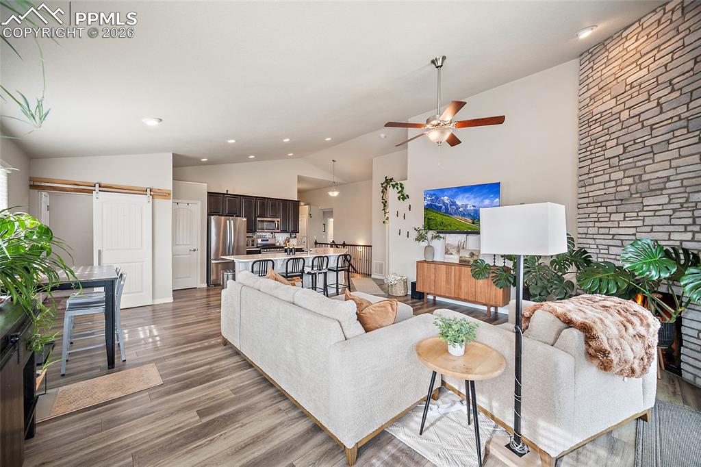 Living room featuring a barn door, wood finished floors, recessed lighting, a ceiling fan, and high vaulted ceiling