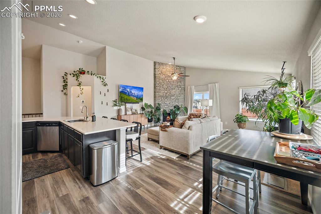 Kitchen featuring vaulted ceiling, dishwasher, wood finished floors, light stone countertops, and open floor plan