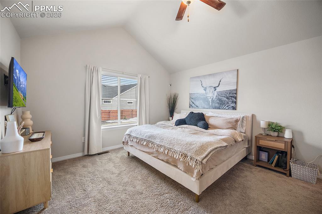 Carpeted bedroom with a ceiling fan and vaulted ceiling