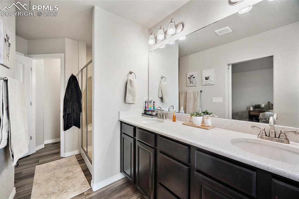 Ensuite bathroom featuring double vanity, a shower stall, and dark wood-style floors