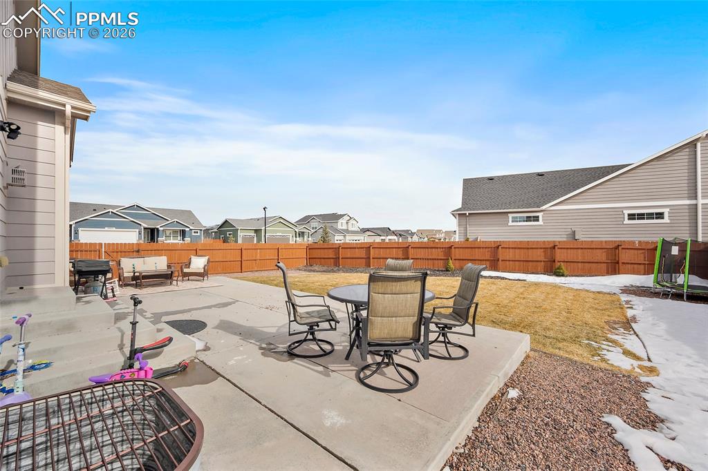 Fenced backyard featuring outdoor dining area, a residential view, a patio, an outdoor hangout area, and a trampoline