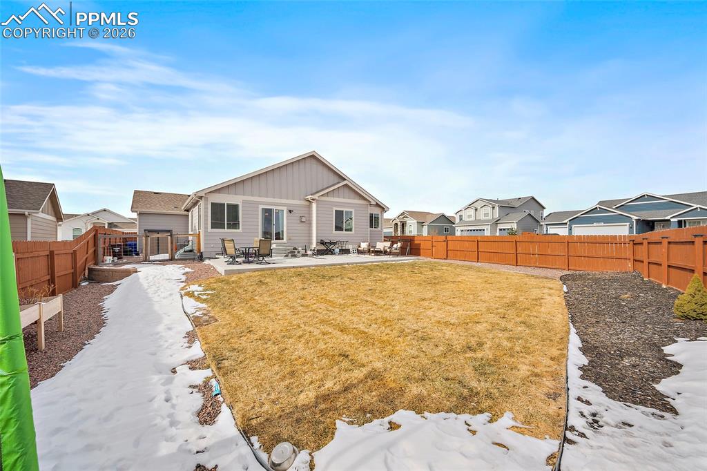 Snow covered property featuring a patio area, a fenced backyard, board and batten siding, and a residential view