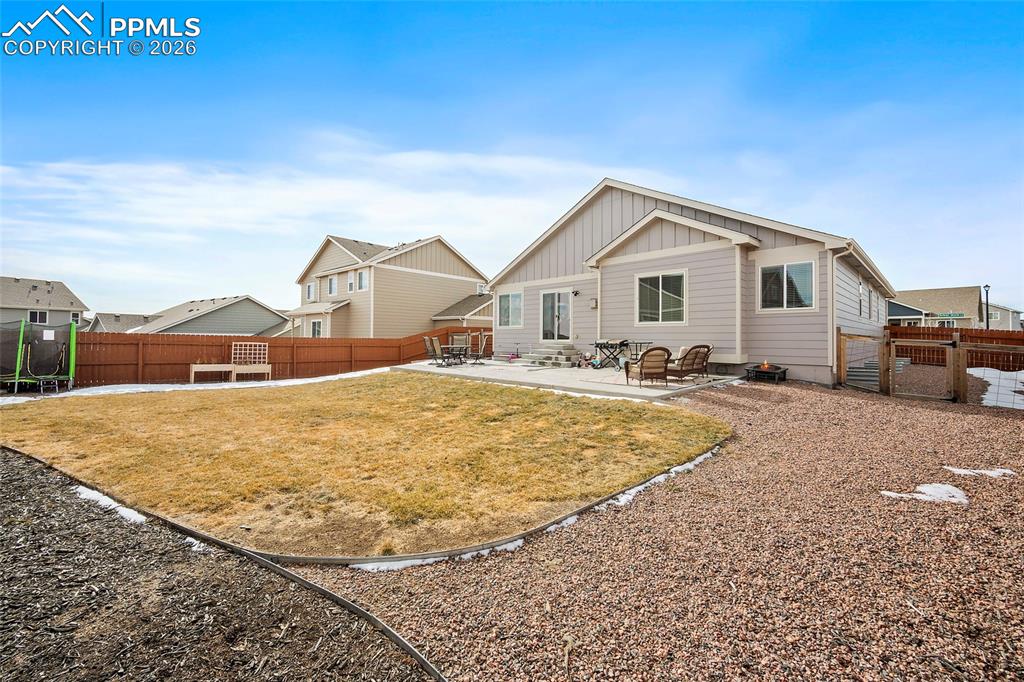 Back of property with a patio, a fenced backyard, board and batten siding, and a trampoline
