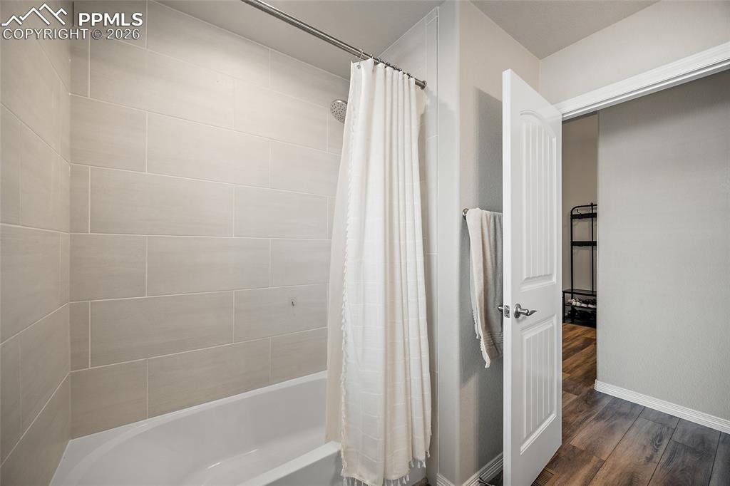 Full bath featuring shower / tub combo and dark wood-style floors