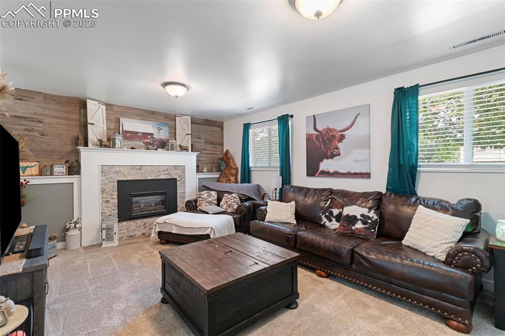 Living room with wooden walls, light colored carpet, and a stone fireplace