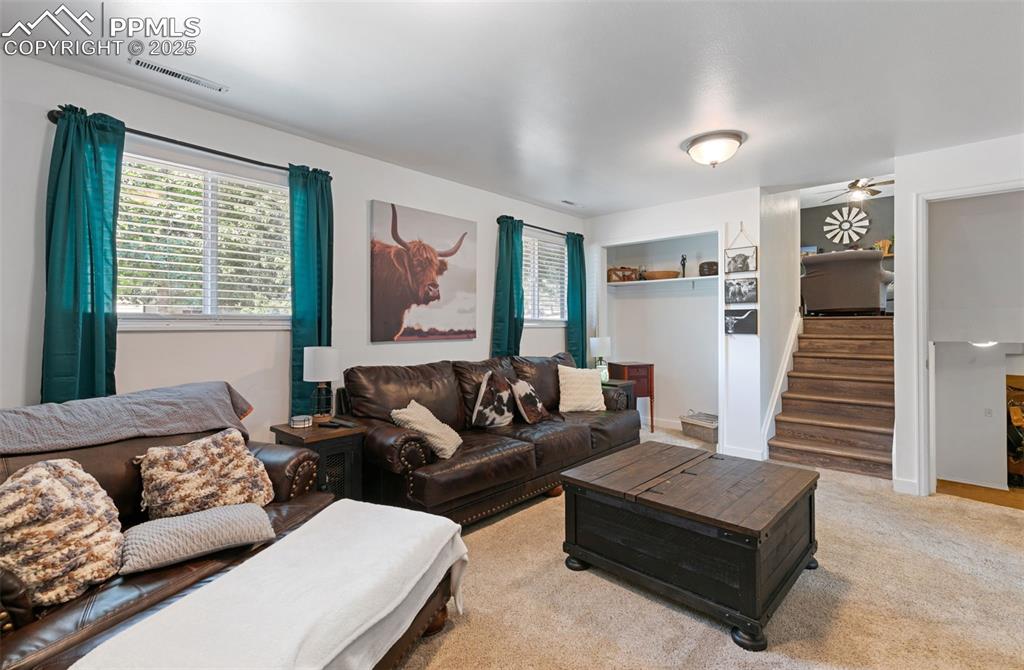 Living area with plenty of natural light, stairs, ceiling fan, and light colored carpet