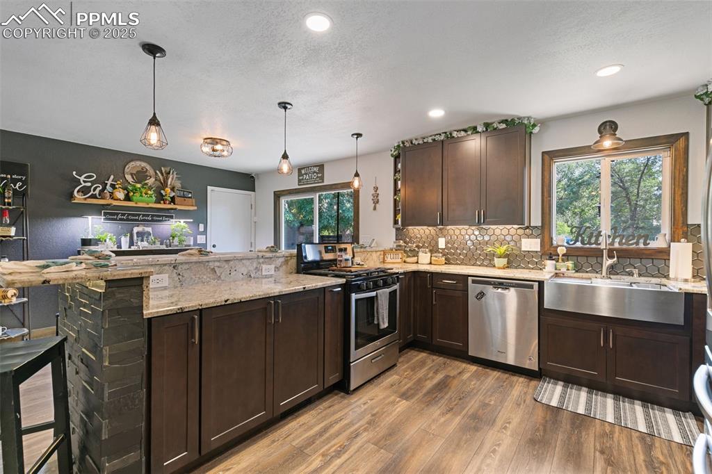 Kitchen featuring dark brown cabinets, a peninsula, appliances with stainless steel finishes, light stone countertops, and dark wood-type flooring