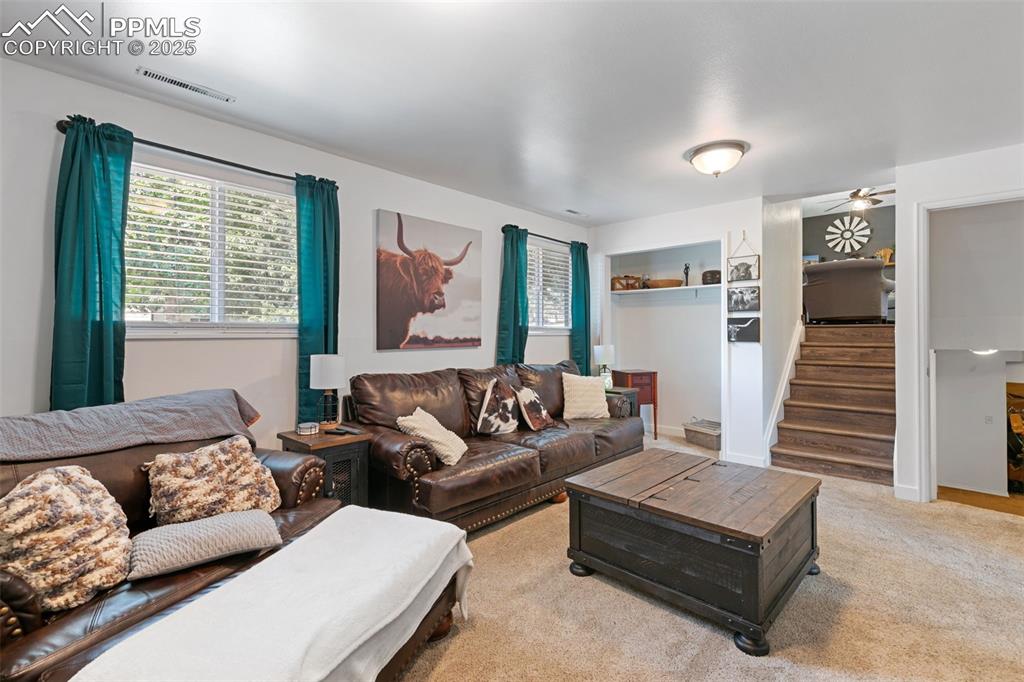 Living area with plenty of natural light, stairway, ceiling fan, and light colored carpet
