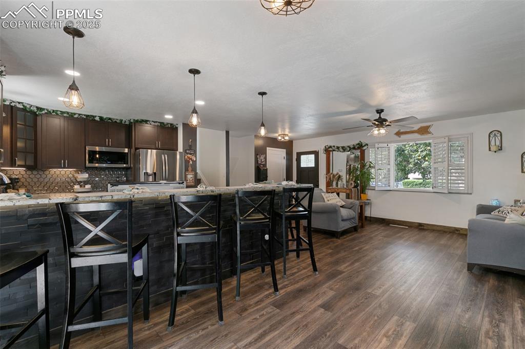 Kitchen featuring a kitchen breakfast bar, glass insert cabinets, dark brown cabinets, light stone counters, and open floor plan