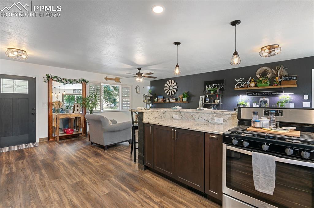 Kitchen with gas stove, dark brown cabinets, light stone countertops, open floor plan, and ceiling fan