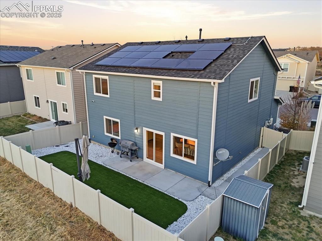 Back of house featuring a patio area, a fenced backyard, roof mounted solar panels, roof with shingles, and a shed