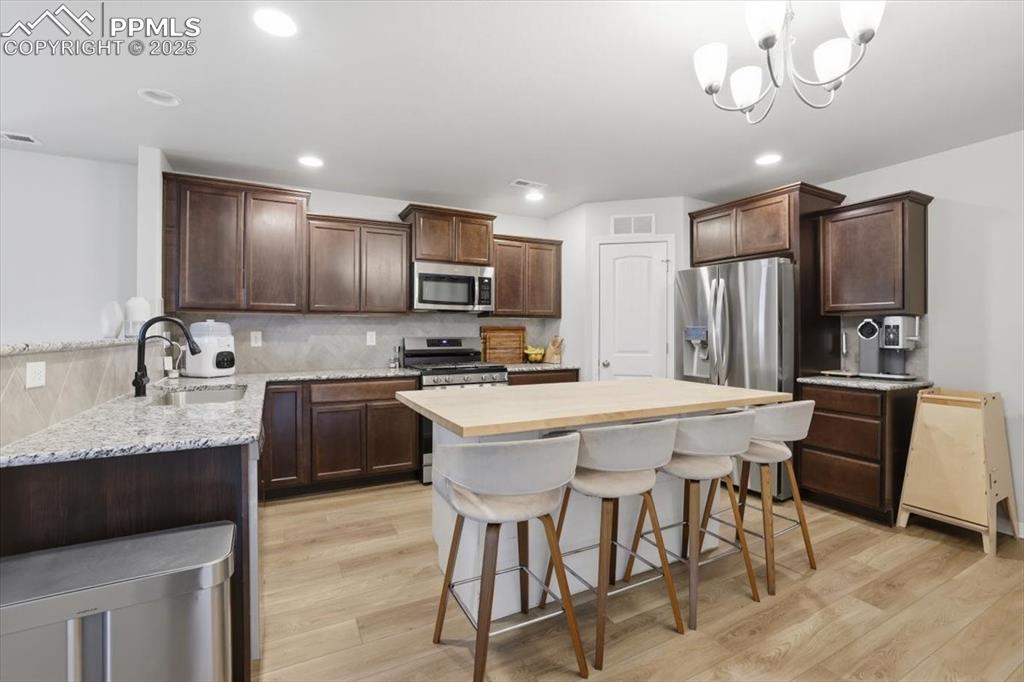 Kitchen featuring dark brown cabinetry, a kitchen bar, butcher block countertops, and recessed lighting