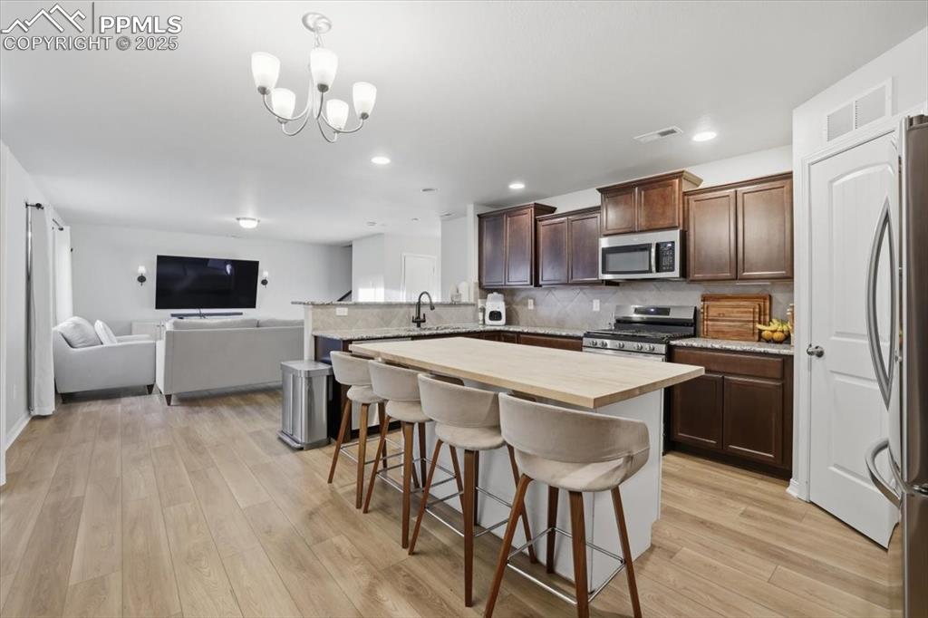 Kitchen with a kitchen breakfast bar, wooden counters, dark brown cabinetry, decorative backsplash, and open floor plan