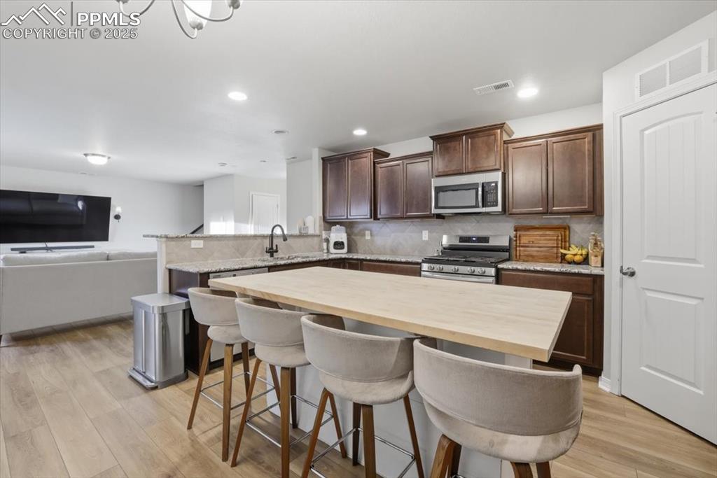 Kitchen with wood counters, a breakfast bar, open floor plan, backsplash, and dark brown cabinetry