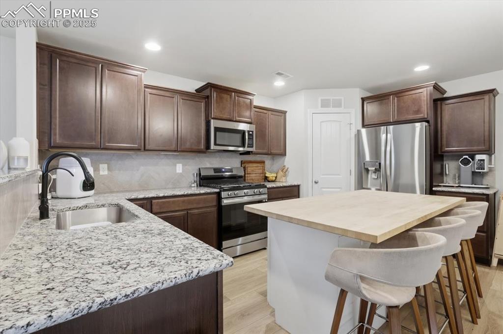 Kitchen with dark brown cabinetry, a kitchen breakfast bar, wood counters, backsplash, and appliances with stainless steel finishes
