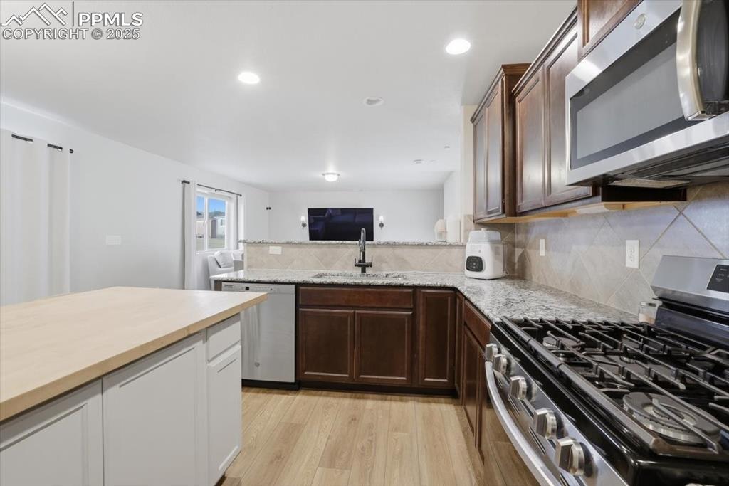 Kitchen featuring stainless steel appliances, tasteful backsplash, light wood finished floors, dark brown cabinetry, and recessed lighting