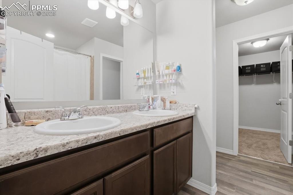 Full bathroom featuring a walk in closet, a shower with curtain, double vanity, and light wood-type flooring