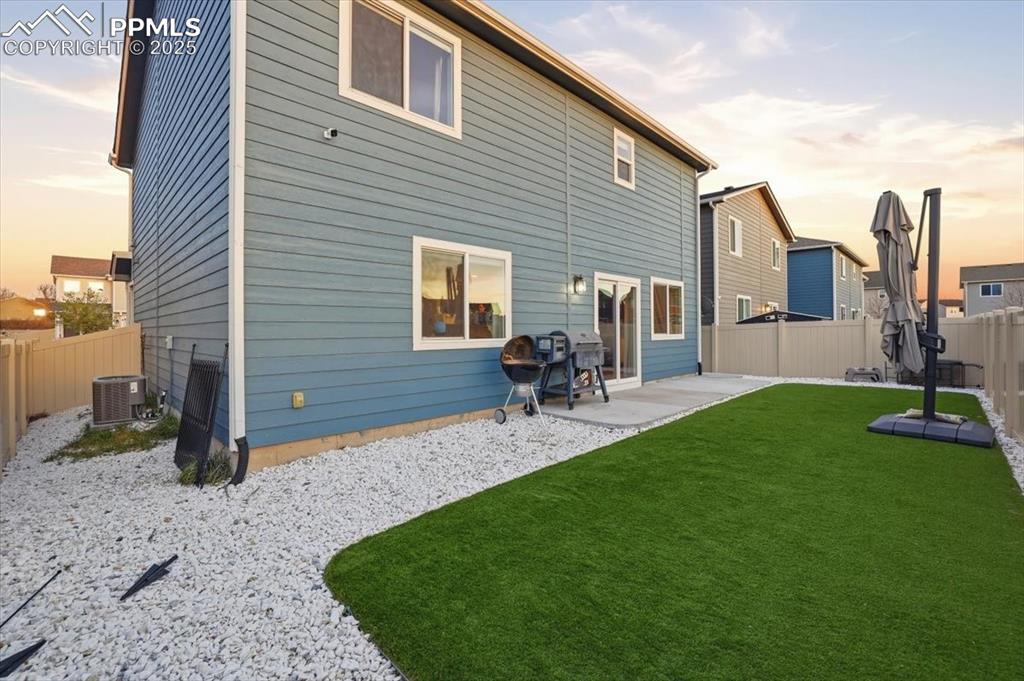 Back of house at dusk with a fenced backyard and a patio