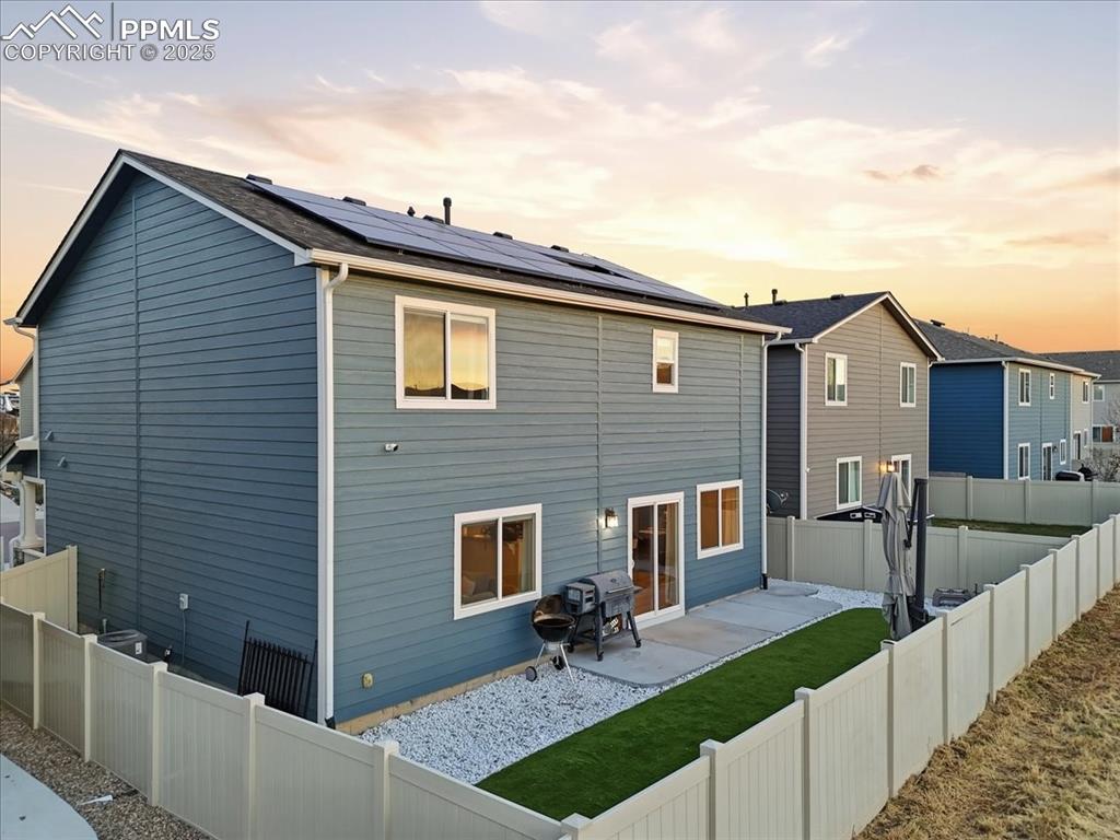 Back of property at dusk with a patio area, a fenced backyard, and solar panels