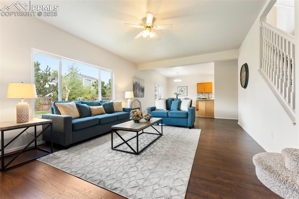 Living room featuring plenty of natural light, dark wood finished floors, a ceiling fan, and stairway