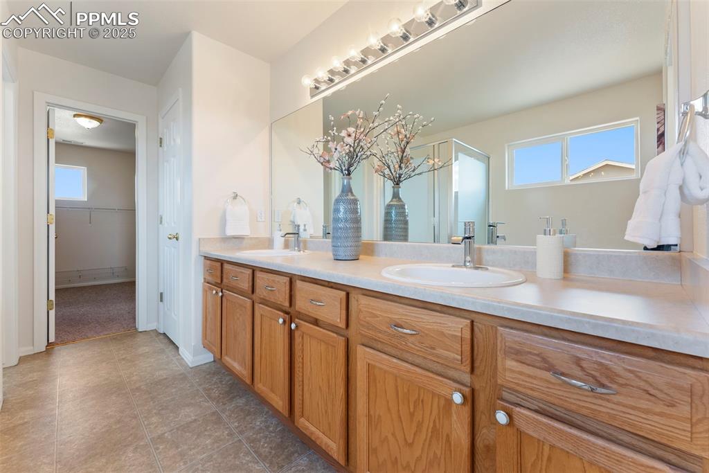 Full bathroom featuring double vanity, plenty of natural light, a spacious closet, and light tile patterned floors