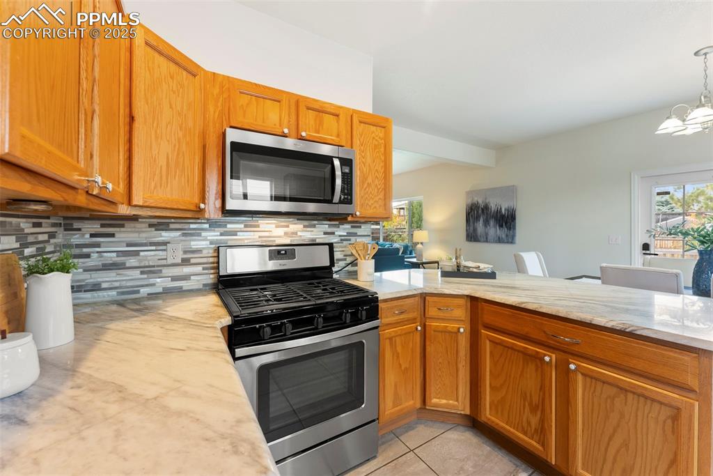Kitchen featuring stainless steel appliances, backsplash, brown cabinets, and light tile patterned floors