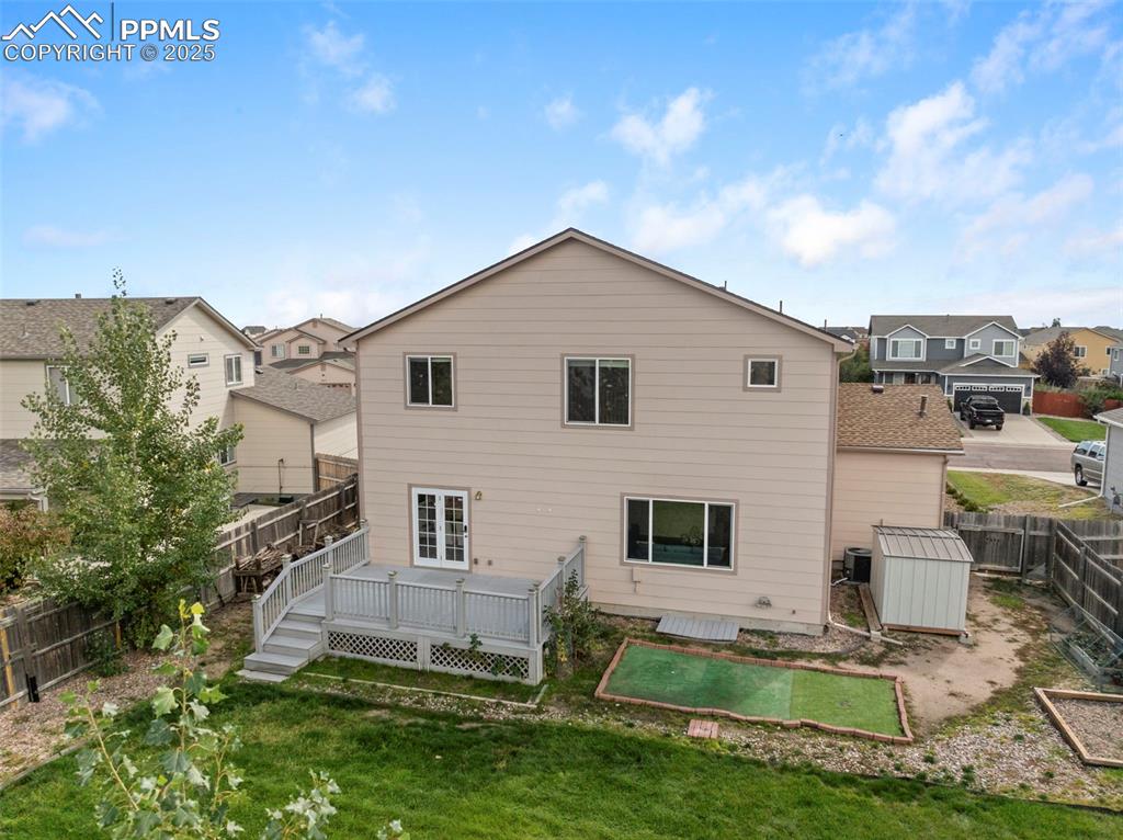 Rear view of property featuring a fenced backyard, a deck, a storage shed, and a residential view