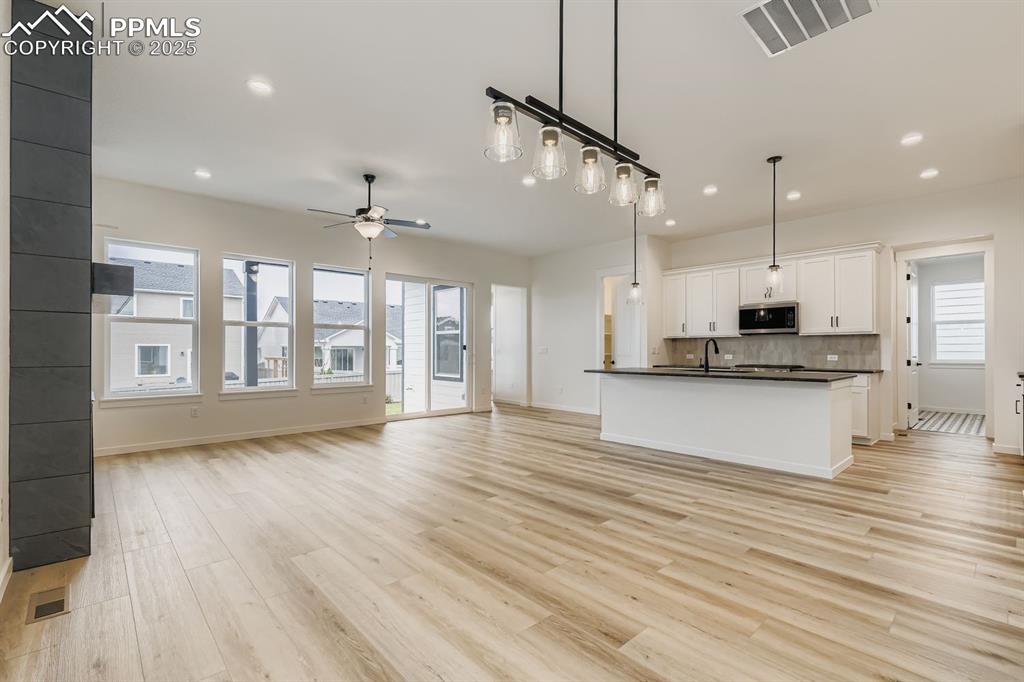Kitchen featuring open floor plan, hanging light fixtures, dark countertops, white cabinets, and an island with sink