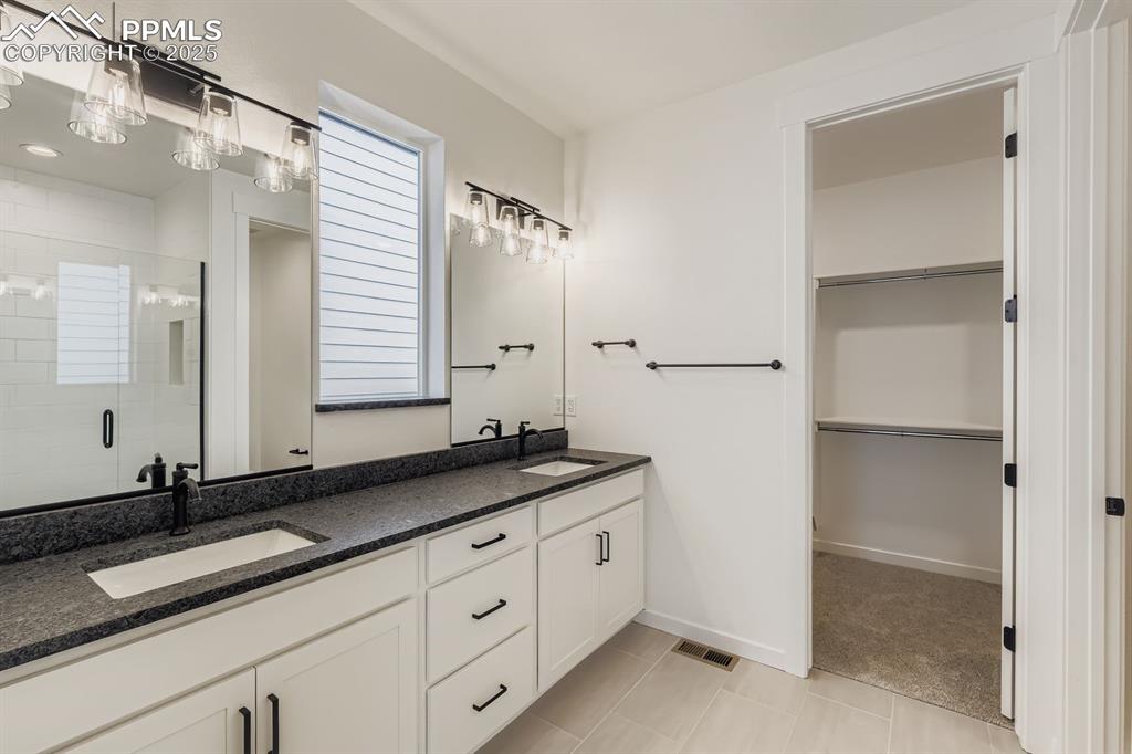 Full bath featuring a spacious closet, a shower stall, double vanity, and plenty of natural light