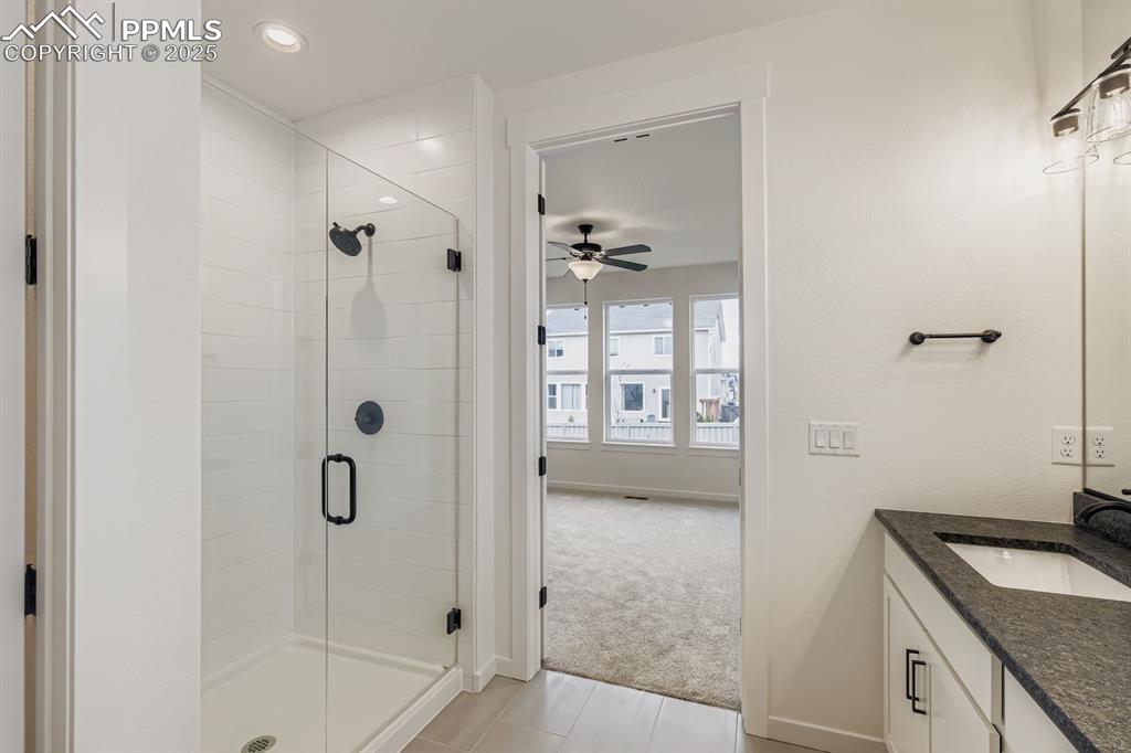 Bathroom featuring a shower stall, vanity, light carpet, light tile patterned floors, and ceiling fan