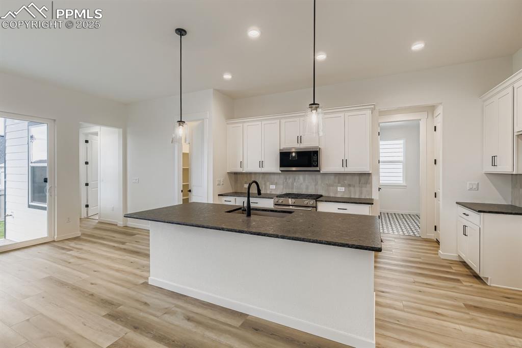Kitchen with white cabinetry, stainless steel appliances, decorative backsplash, an island with sink, and recessed lighting