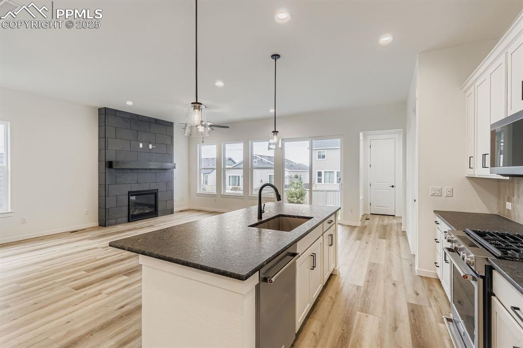 Kitchen featuring appliances with stainless steel finishes, hanging light fixtures, white cabinetry, a large fireplace, and recessed lighting