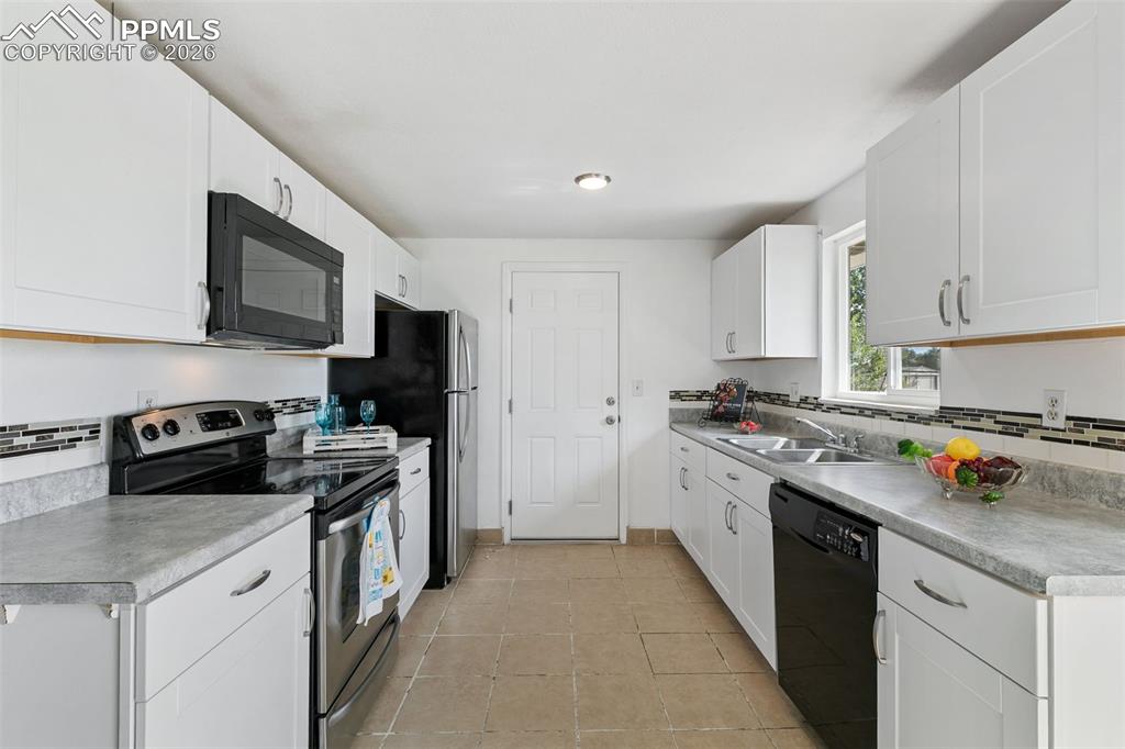 Kitchen with black appliances, white cabinets, decorative backsplash, and light countertops