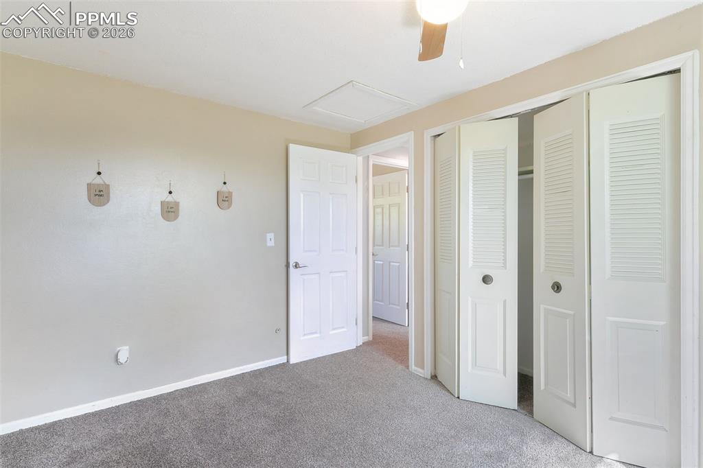 Unfurnished bedroom featuring carpet flooring, attic access, a closet, and a ceiling fan