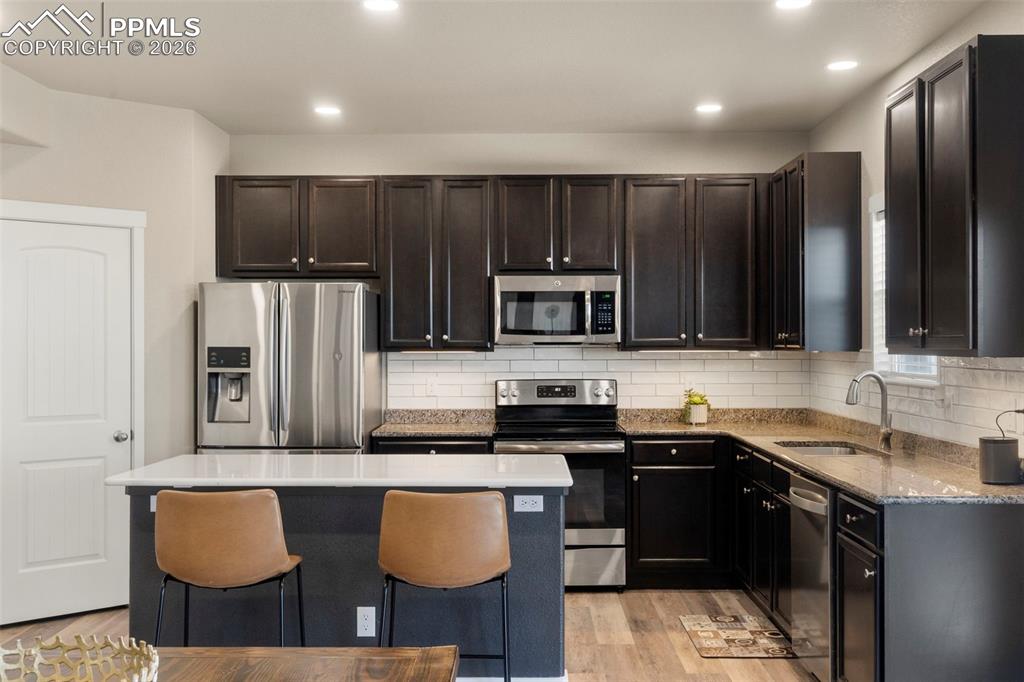 Kitchen featuring stainless steel appliances, light wood-style flooring, a center island, a kitchen breakfast bar, and light stone counters