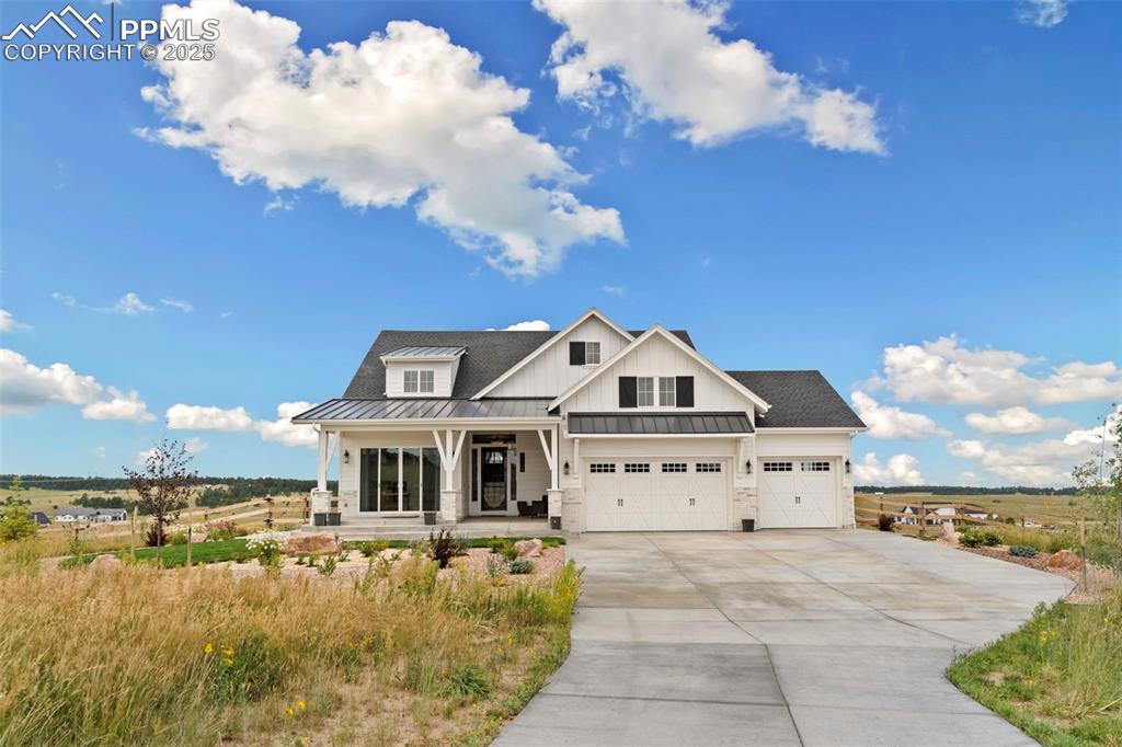 View of front of home featuring covered porch, a standing seam roof, a metal roof, driveway, and a garage