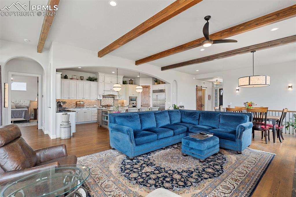 Living room featuring arched walkways, dark wood-type flooring, recessed lighting, ceiling fan, and beamed ceiling