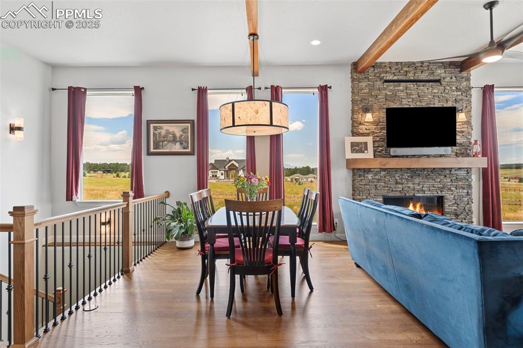 Dining room with a stone fireplace, wood finished floors, healthy amount of natural light, and beamed ceiling