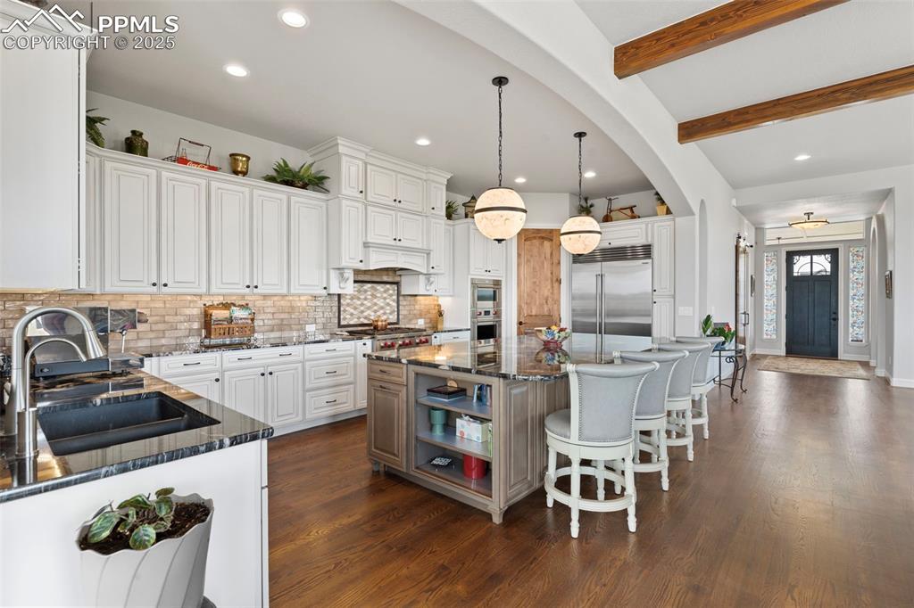 Kitchen featuring beam ceiling, a breakfast bar, dark stone counters, decorative backsplash, and decorative light fixtures