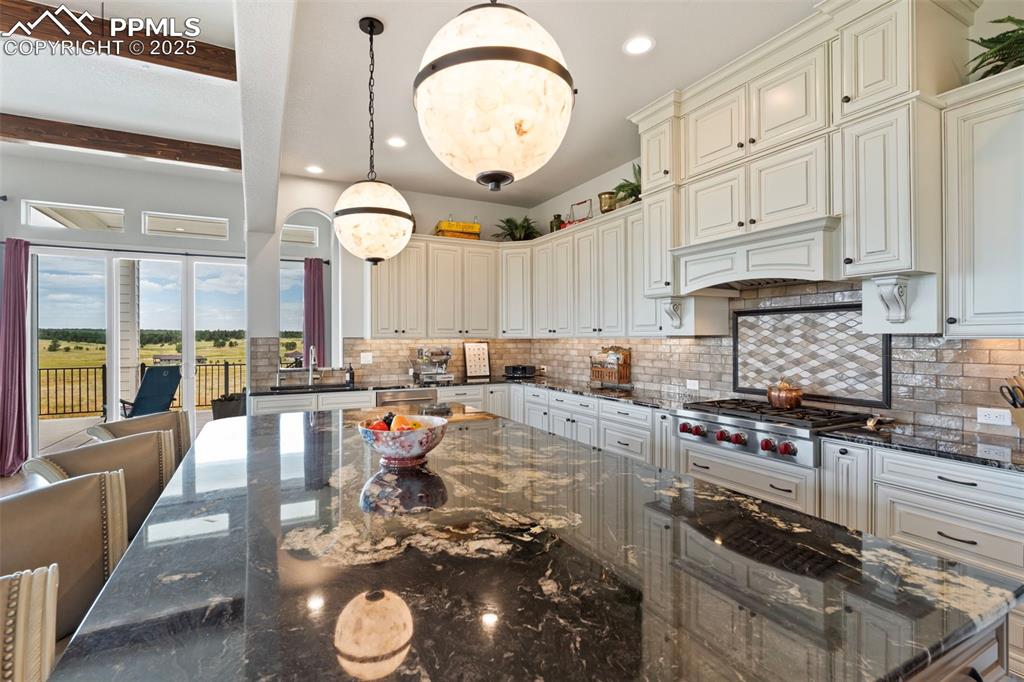 Kitchen featuring dark stone counters, decorative light fixtures, decorative backsplash, stainless steel gas stovetop, and beamed ceiling