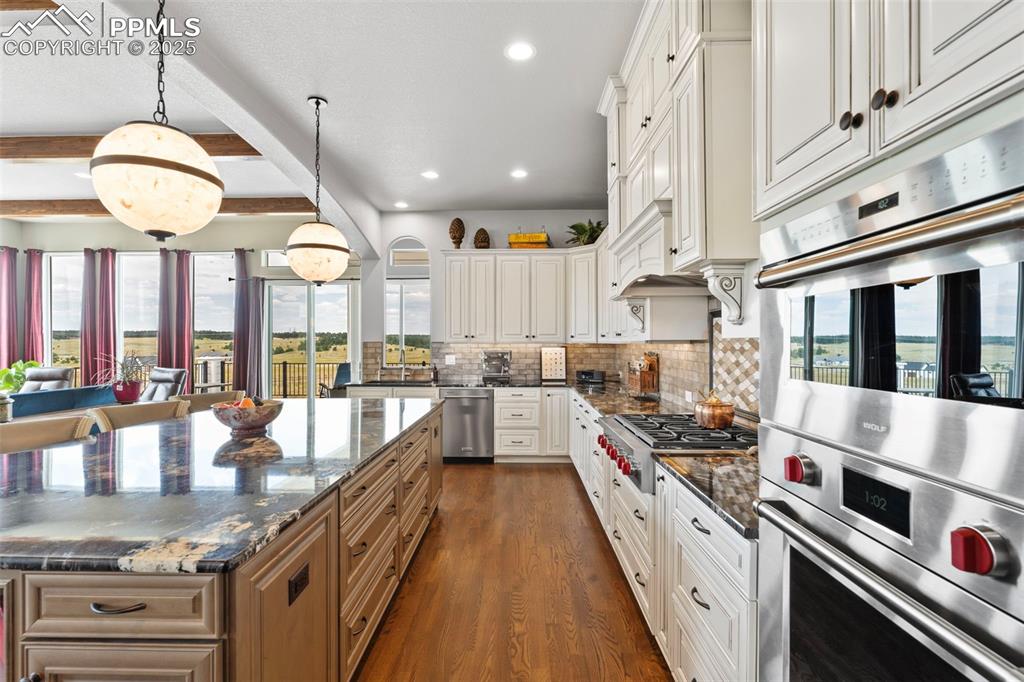 Kitchen featuring stainless steel appliances, decorative light fixtures, beam ceiling, dark wood-style flooring, and recessed lighting