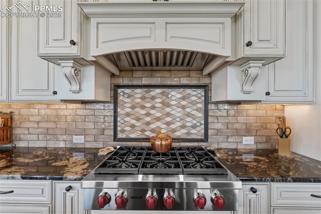 Kitchen with dark stone counters, decorative backsplash, and white cabinetry