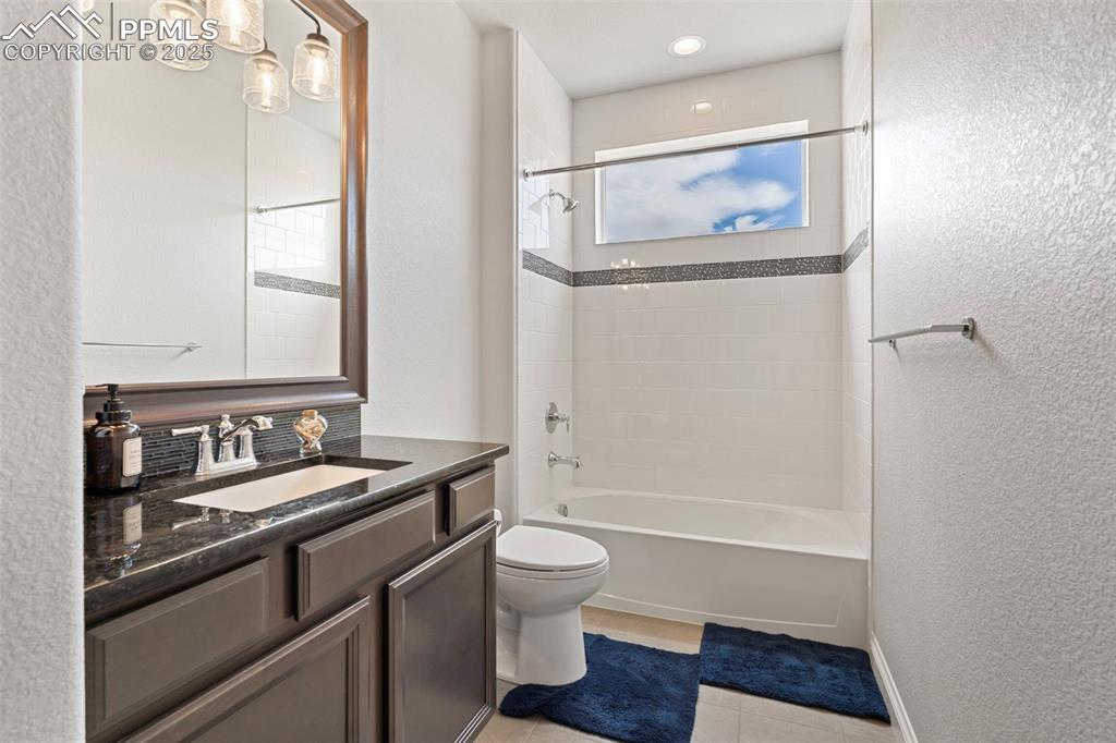 Bathroom with a textured wall, shower / bath combination, vanity, and light tile patterned floors