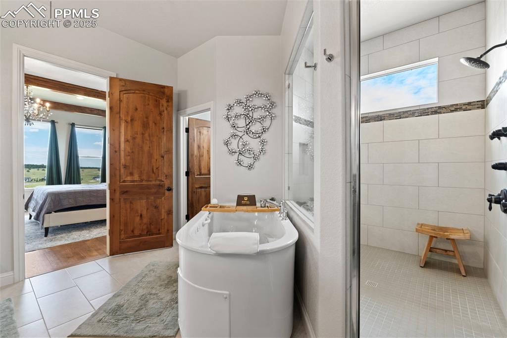 Bathroom featuring a stall shower, light tile patterned floors, a freestanding tub, and connected bathroom
