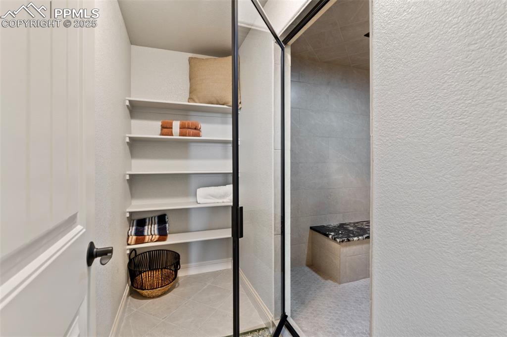 Bathroom with a textured wall, light tile patterned floors, and a stall shower